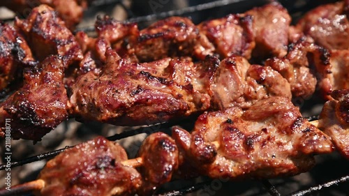 Grilled meat skewers cooking on barbecue grill with smoke and charred texture
