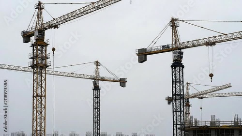 Multiple Construction Cranes Silhouetted Against A Gray Sky Showcasing Industrial Development And Urban Growth In The Heart Of The City