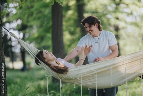 Photography A young couple relaxes in a hammock while the man smiles and interacts with the woman