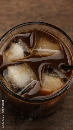 Coffee with ice. Hand stirring coffee with ice in glass with black straw, close up