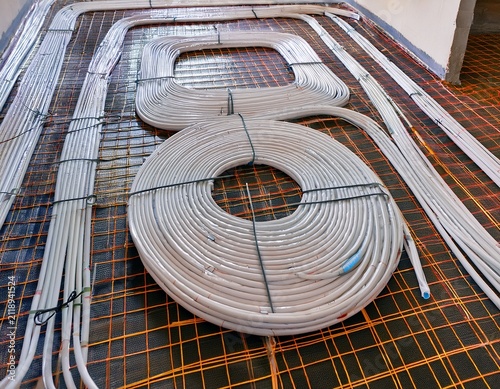 heating system installation with white tubing coiled on the floor laid out in a grid pattern on a construction site for underfloor heating system
