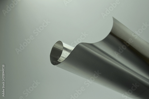 a sample of thin silver aluminum sheet on a blurred background with smooth curved folds. a bright, lightweight metal material.