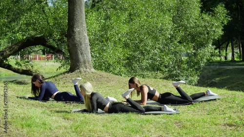 Three women stretch gracefully on mats in morning park. Atmosphere is filled with energy and tranquility as they practice their routines in fresh air. 4K, UHD