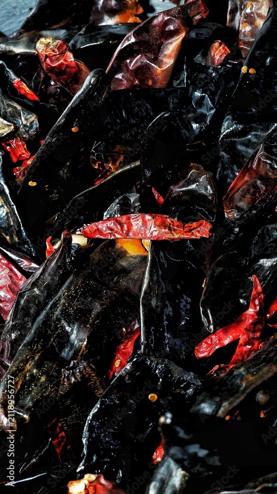 Naklejka premium Close-up of assorted dried Mexican chili peppers with rich natural textures and deep red and dark tones. Traditional culinary ingredients commonly used in authentic sauces, marinades, and regional cui