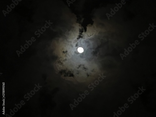 Fotografie Mystical full moon shining through dark clouds at night, glowing lunar sphere in