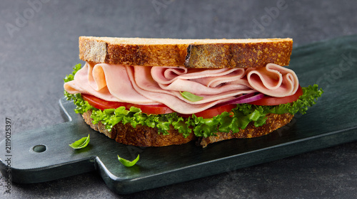 Fresh ham sandwich with tomato lettuce and red onion on toasted artisan bread. Grey background. Close up.