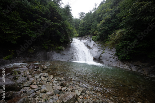 Serene waterfall cascading over smooth granite rocks into emerald green pool surrounded by lush green forest in Japan