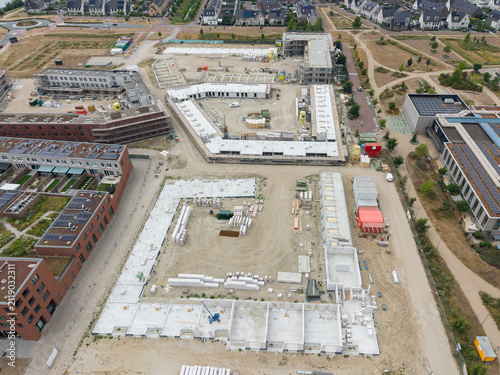 Aerial view of a construction site featuring building foundations, concrete slabs, and various materials in a developing residential area in the Netherlands.