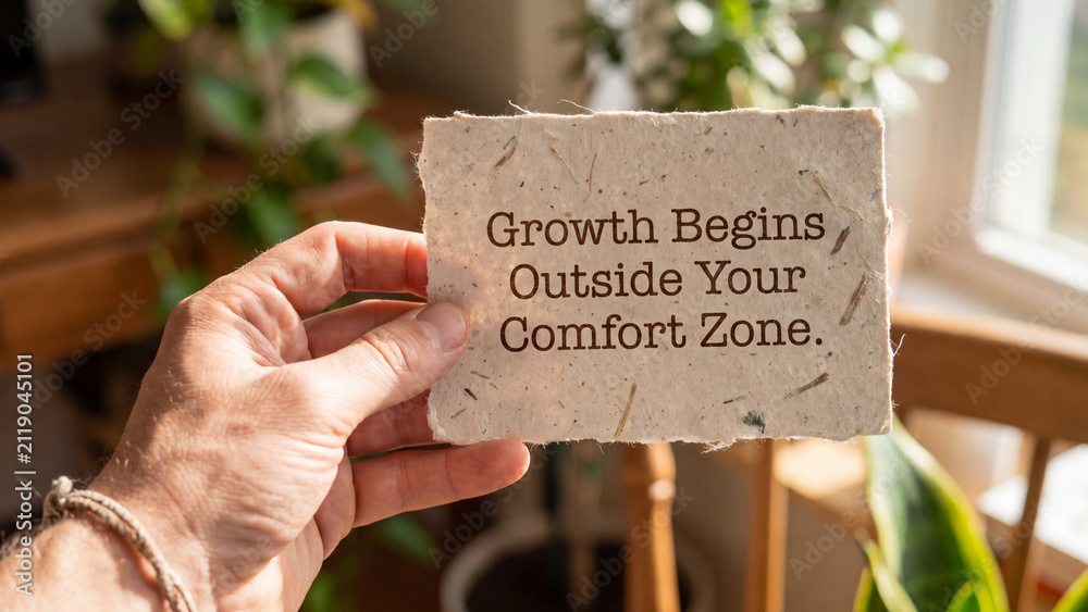 Fototapeta premium Hand holding a piece of handmade paper with the text growth begins outside your comfort zone written on it
