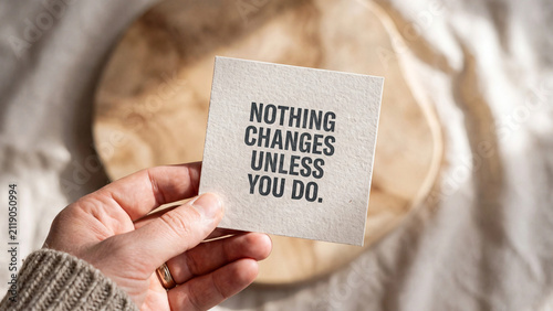 Hand holding a small square card with the inspirational quote nothing changes unless you do printed on textured paper