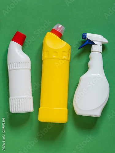 Collection of household cleaning bottles arranged on a green backdrop, representing domestic cleaning, disinfecting, surface care, and everyday home maintenance.