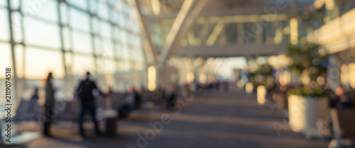 A blurred view of a spacious airport terminal with large windows, showcasing an airy atmosphere filled with travelers and modern architecture.