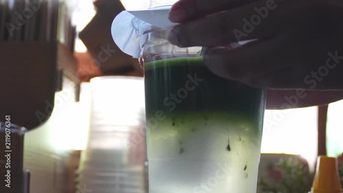 4K Barista closing plastic lid on iced layered matcha green tea cup at cozy cafe counter, Concept for beverage packaging takeaway drink matcha coconut and cafe service.