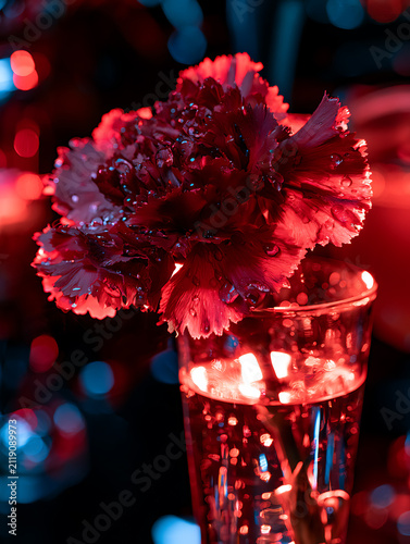 Deep red carnations placed on a bar table illuminated by neon lights