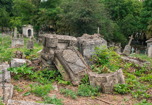 Foto Crumbling stone monuments scattered across ancient overgrown cemetery during day