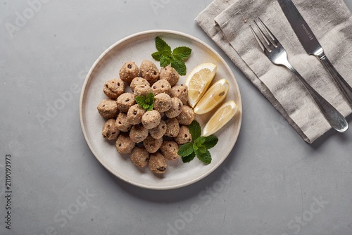 Kibbeh made with bulgur shells and spiced lamb filling, garnished with fresh herbs on grey concrete surface. Concept of Mediterranean cuisine, showcasing traditional flavors and textures.