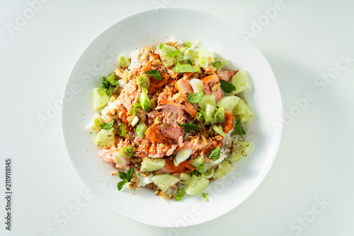 Baked salmon salad with cucumbers, chickpeas, walnuts, feta and rice on white background