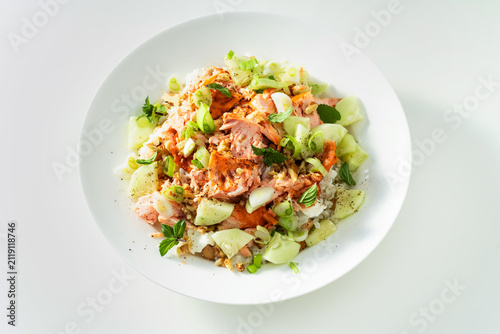 Baked salmon salad with cucumbers, chickpeas, walnuts, feta and rice on white background
