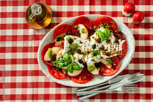 Italian style salad with tomatoes, peaches, olives, burrata and pesto on a set dining table
