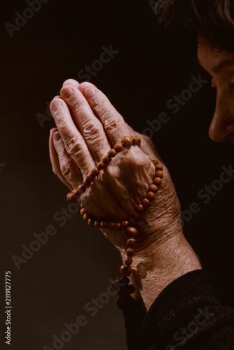Quadro su tela An elderly woman holds a wooden rosary with cross in her hand