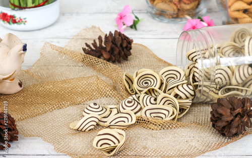 Bild auf Leinwand A traditional Indonesian sweet snack, kuping gajah—crispy, spiral-shaped cookies resembling elephant ears—spilled from a clear glass cookie jar