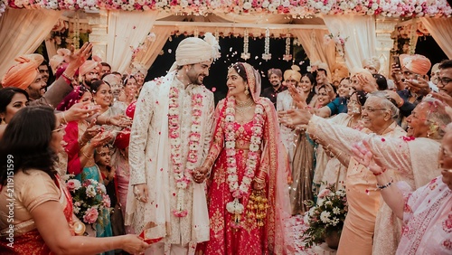 Indian wedding celebration, bride and groom arrival ceremony, traditional wedding couple entering venue, guests throwing flower petals, festive cultural event moments