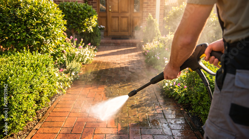 Professional worker using high pressure water jet cleaner on brick garden pathway for outdoor maintenance home improvement and exterior cleaning service with cleaning pressure maintenance