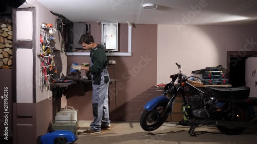 Mechanic working on a motor vehicle engine part with hand tools at a workbench in a home garage, performing maintenance and repair work on a vintage motorcycle