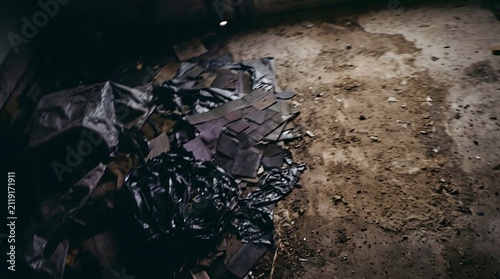A dimly lit industrial interior featuring a rough concrete floor with scattered debris and shadows cast by overhead lighting in a dark abandoned warehouse