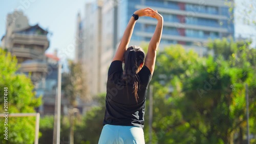 Woman, stretching and back view in city with fitness, flexibility or wellness outdoor. Rear view, athlete or person with arms overhead, smart watch and workout warm up in park.