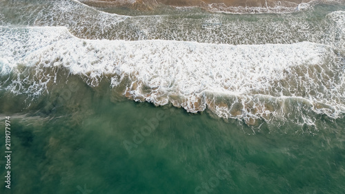 Top down aerial view of emerald sea waves washing ashore with white foam on sandy beach in Greece for ocean nature travel stock photo background concept texture