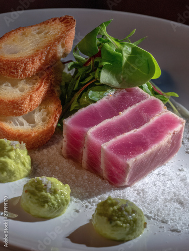 render of an elegant lunch pairing. A starter of avocado toast slices sits next to a main dish of pan-seared tuna with garden greens. The lighting is soft and bright, highlighting the fresh 