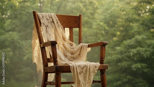 Rustic wooden chair draped with delicate sheer fabric in a sunlit forest nature setting soft ethereal light