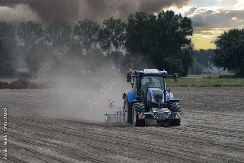 Принти на полотні Blue tractor working on dry dusty farmland, raising dust while cultivating a fie