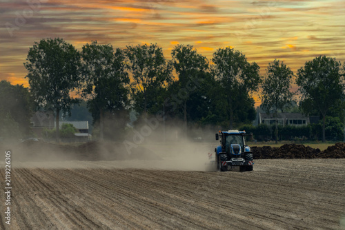 Blue tractor working on dry dusty farmland, raising dust while cultivating a field in rural agricultural landscape