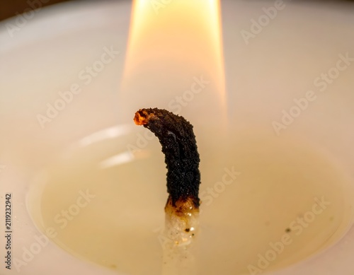 Macro photo of a burning candle wick with a bright flame in a wax pool