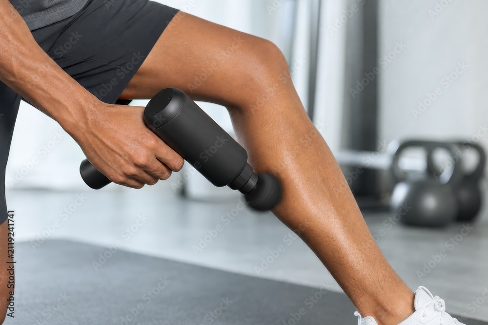 Fototapeta premium Person using percussion massage gun on calf muscle