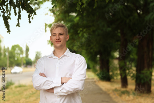 Portrait of handsome man wearing white shirt with crossed arms in park. Space for text