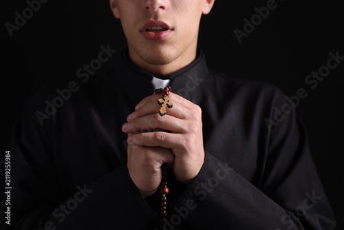 Photography Priest with rosary praying on black background, closeup