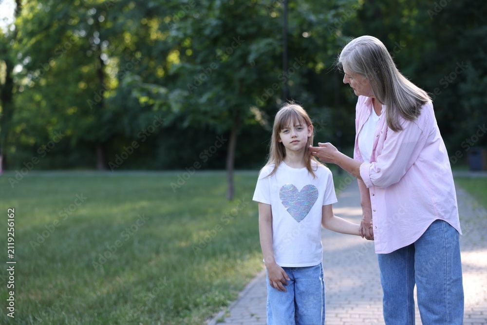 Fototapeta premium Grandmother and granddaughter holding hands while walking in summer park. Space for text