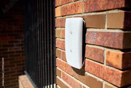 Принти на полотні Sunlit red brick exterior wall with white rectangular wall mounted control panel