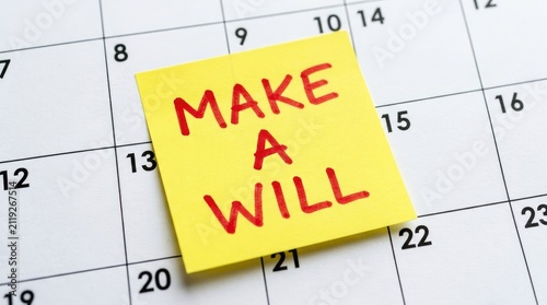 Yellow sticky note with red handwritten text stating make a will placed on white calendar