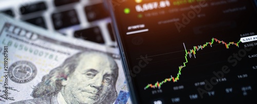 Digital chart rises beside dollar bills and keyboard. Viewer sees growth and financial data in focus. No people shown, no emotion to convey. Use for finance, investment, or tech business concepts
