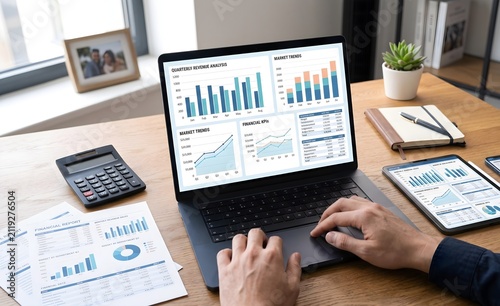 Professional working on a laptop analyzing financial charts and business data at a wooden office desk