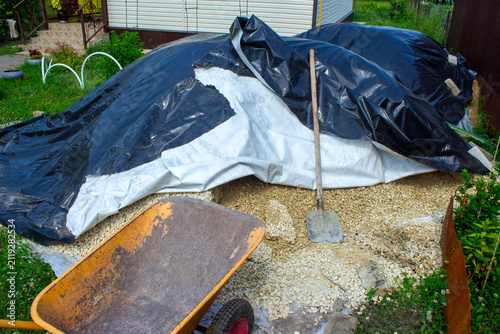 Куча щебня накрыта клеенкой, лопата и садовая тачка.A pile of rubble is covered with oilcloth, a shovel and a garden wheelbarrow.