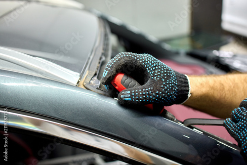 Fotografie Mechanic removing windshield trim from dark car with power tool and gloved hand