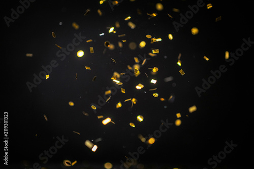 Numerous golden shiny confetti pieces in various shapes including rectangles circles and stars are gracefully falling and scattering through the air creating a festive and celebratory atmosphere