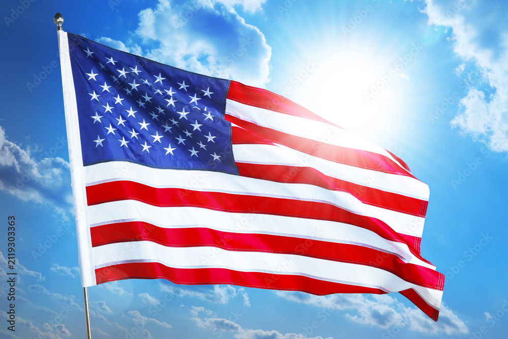 Fototapeta premium American flag waving against bright sun in blue sky