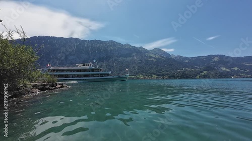 Tour boat cruising on turquoise Thunersee with Swiss alpine mountains under bright clear summer sky