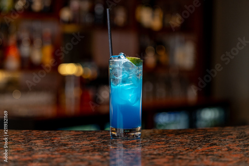 View of a refreshing blue cocktail served in a tall glass with ice and a lime wedge on a polished bar counter in Asker, Akershus, Norway.